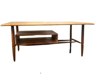 May include: A mid-century modern coffee table with a light wood top and a lower shelf. The table has a simple, elegant design with tapered legs.