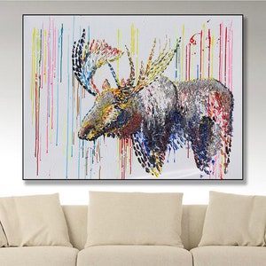 May include: Abstract painting of a moose with colourful paint drips. The moose is depicted with textured brushstrokes in shades of brown, blue, yellow, and red against a white background. The artwork is framed in a black frame.