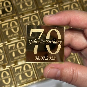 Może przedstawiać: Kolekcja kwadratowych złotych płytek akrylowych z liczbą 70, napisem Gabriel's Birthday oraz datą 08.07.2028. Każdy element ma odblaskową powierzchnię z wzorem wygrawerowanym w ciemnym, kontrastującym odcieniu.