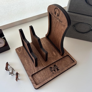 May include: A wooden phone and headphone stand with the name "Oliver Miller" and a monogram. The stand is stained a dark brown with black accents. A small clock and miniature animal figurines are also present.