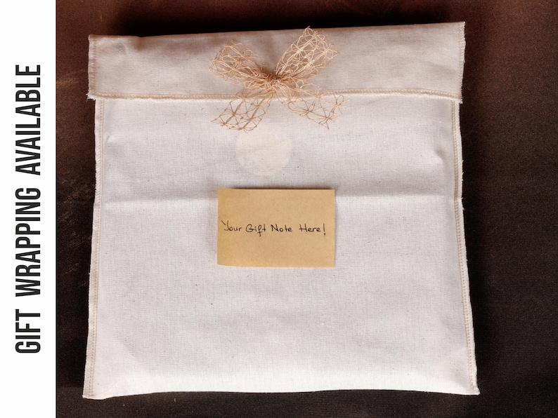 May include: A white fabric gift bag with a beige bow and a small, rectangular card that reads "Your Gift Note Here!". The bag is closed at the top and sits on a dark brown surface.