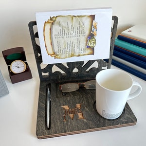 May include: A dark wood desk organiser with a personalised name, "James", engraved on the front. It features a built-in pen holder, a slot for glasses, and a cup holder. The organiser is displayed on a white surface with a stack of books and a small clock.