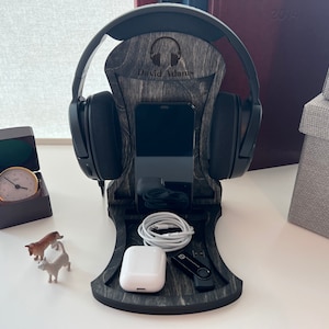 Pode incluir: Um suporte para fones de ouvido de madeira com acabamento em madeira preto e cinza. O suporte tem um suporte para telefone, um espa&ccedil;o para fones de ouvido e uma unidade USB. O suporte &eacute; personalizado com o nome "David Adams".