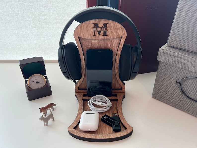 Pode incluir: Suporte de madeira para fones de ouvido com um suporte para telefone, uma pequena caixa de carregamento sem fio branca e uma unidade USB preta. O suporte &eacute; personalizado com o nome "Oliver" e a inicial "M".