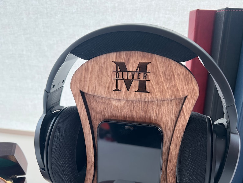Pode incluir: Suporte de madeira para fones de ouvido com um suporte para telefone. O suporte &eacute; personalizado com a letra "M" e o nome "Oliver" gravado nele.