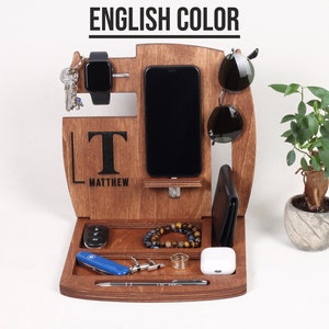May include: A wooden organiser with spaces for a phone, watch, keys, sunglasses, wallet, and other accessories. The organiser is engraved with the name "Matthew" and the initial "T". A small plant in a decorative pot is on the right.
