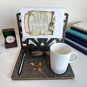 May include: A dark wood desk organiser with a personalised name "JAMES M" engraved on the front. It features a pen holder, a glasses holder, a mug holder, and a book stand.