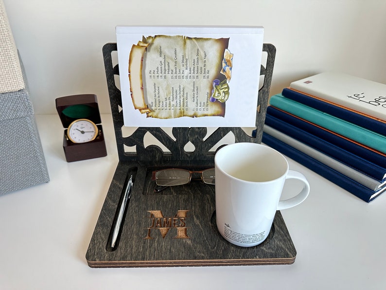 May include: A dark wood desk organiser with a personalised name "JAMES M" engraved on the front. It features a pen holder, a glasses holder, a mug holder, and a book stand.