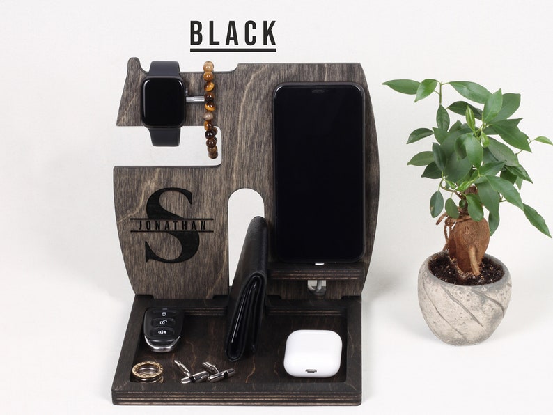 K&ouml;nnte beinhalten: Ein Holzorganizer mit schwarzer Oberfl&auml;che. Er hat F&auml;cher f&uuml;r ein Telefon, eine Uhr und eine Brieftasche. Der Organizer hat auch ein kleines Fach f&uuml;r Schl&uuml;ssel und andere Kleinigkeiten. Der Organizer ist mit dem Namen "Jonathan" und dem Initial "S" personalisiert.