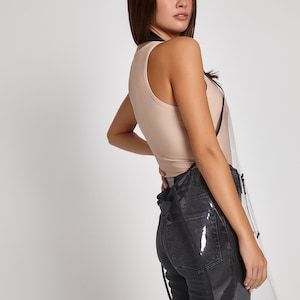 May include: A clear plastic apron with black trim and adjustable straps. The apron is worn over a beige tank top and black jeans.