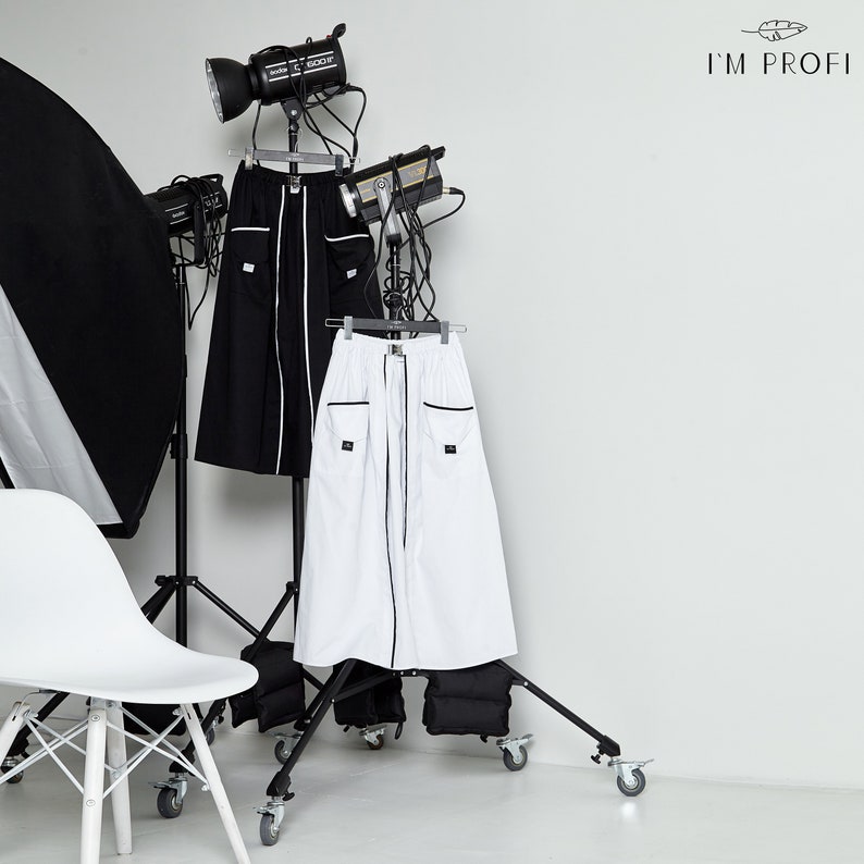 May include: Two long skirts, one black and one white, are displayed on a clothing rack. Both skirts have black trim and pockets. The skirts are on a white background with the text "I'M PROFI" in the top right corner.