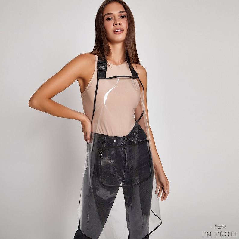 May include: A clear plastic apron with black straps and a black pocket. The apron is worn over a beige tank top and black jeans.
