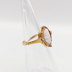 May include: A gold ring with a cameo featuring a white profile portrait surrounded by small white gemstones.