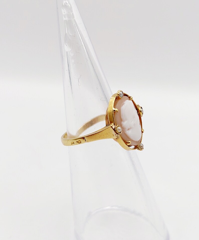 May include: A gold ring with a cameo featuring a white profile portrait surrounded by small white gemstones.