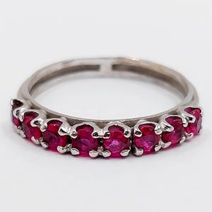 Op de afbeelding: Een zilveren ring met een rij rode robijnen.