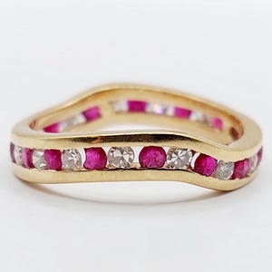 May include: A gold band ring with a wavy design. The ring is set with alternating red rubies and clear diamonds.