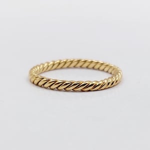 Peut inclure: Une bague fine et circulaire en or jaune poli. L'anneau présente une texture torsadée continue et répétitive qui fait tout le tour de la circonférence, créant un aspect uniforme et texturé avec une finition brillante et réfléchissante.