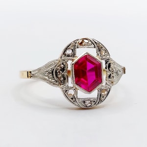 Peut inclure: Une bague ancienne ornée d'un rubis hexagonal vif en son centre. Le rubis est serti dans un motif filigrané orné de petits diamants. La monture est en or et le sertissage est de couleur argentée.