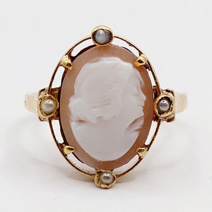 May include: Gold ring with a cameo featuring a woman's profile. The cameo is set in a gold frame with three small pearls on each side.