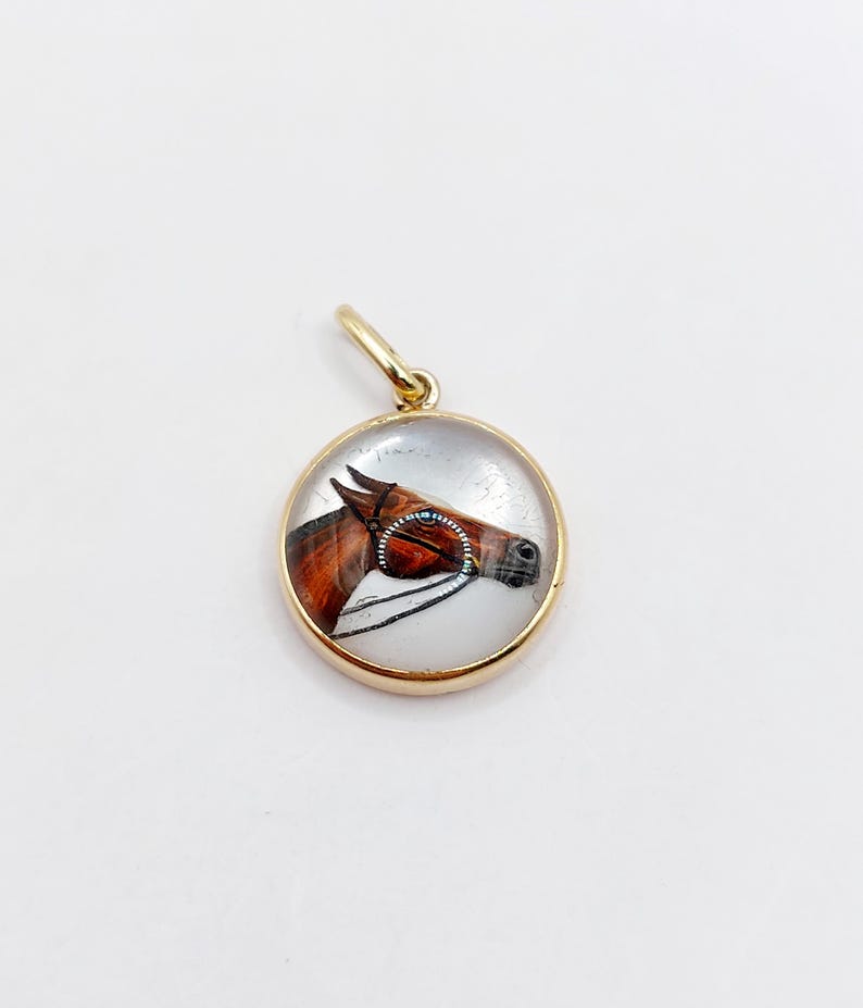 May include: A gold-toned pendant with a glass oval featuring a painted image of a brown horse's head with a bridle.