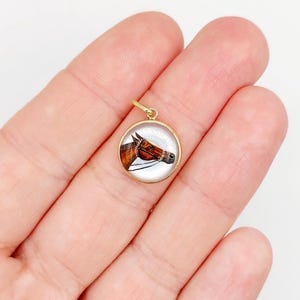 May include: A gold pendant with a round glass cabochon featuring a hand-painted portrait of a brown horse's head.