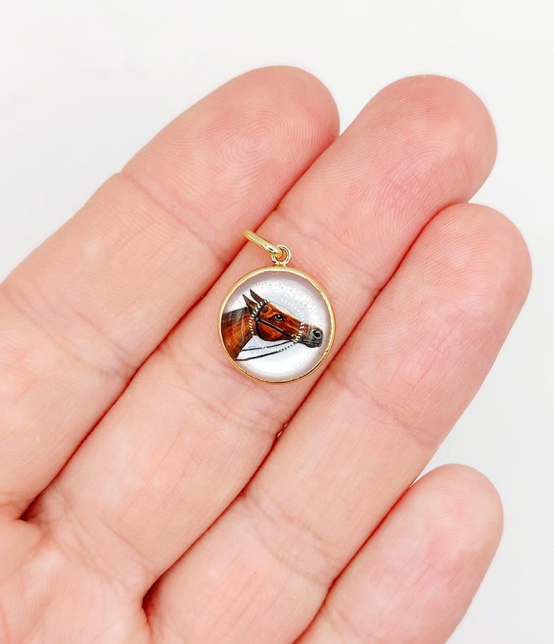 May include: A gold pendant with a round glass cabochon featuring a hand-painted portrait of a brown horse's head.