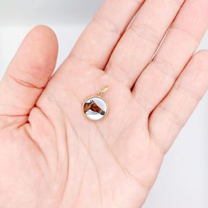 May include: A gold pendant featuring a hand-painted portrait of a brown horse's head. The pendant is round and has a white background.