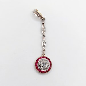 Peut inclure: Pendentif vintage avec un motif circulaire, une bordure de pierres rouges et un groupe de pierres claires au centre. Il est suspendu à une chaîne argentée avec des détails décoratifs et une bélière dorée.