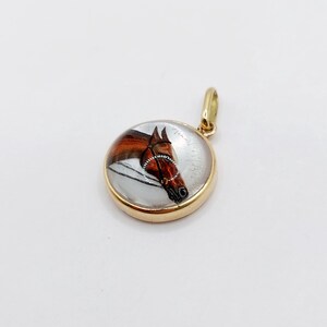 May include: A gold pendant with a glass cabochon featuring a hand-painted image of a brown horse's head.