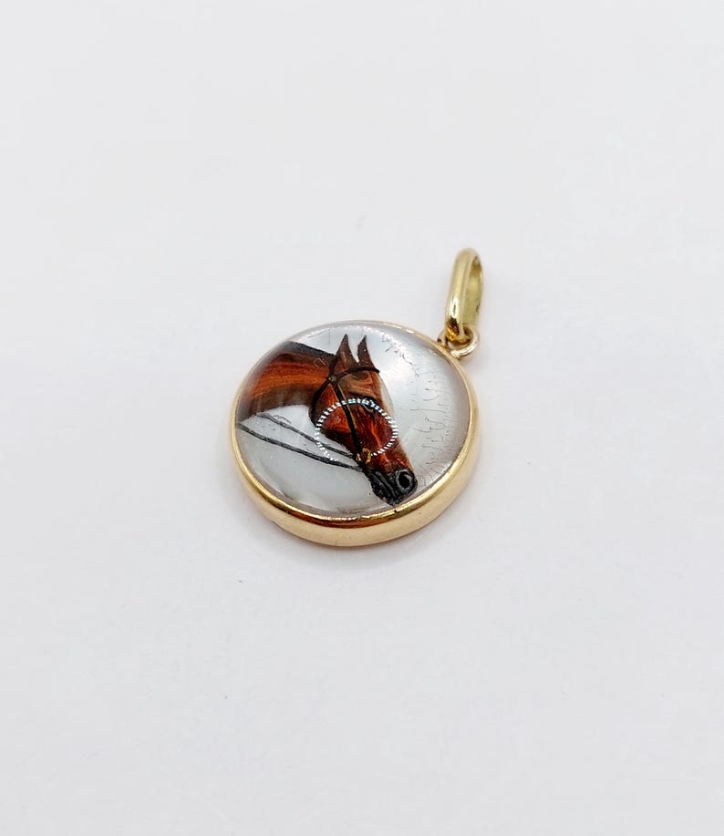 May include: A gold pendant with a glass cabochon featuring a hand-painted image of a brown horse's head.