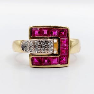 Puede incluir: Un anillo de oro con un diseño cuadrado, engastado con vibrantes piedras preciosas rosas de talla cuadrada. Una sección rectangular con pequeñas piedras preciosas transparentes está engastada en el lateral. El anillo tiene un estilo clásico y elegante.
