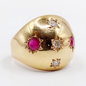 May include: A gold ring with a rounded shape, featuring star-shaped settings with red and clear gemstones. The ring has a polished finish and a classic design, suitable for various occasions.