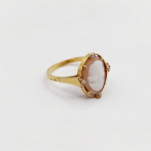 May include: A gold ring with a cameo featuring a white profile portrait set in a shell-like background. The cameo is surrounded by small pearl-like stones.