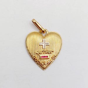 Peut inclure: Un pendentif en forme de cœur en or avec une texture striée verticale. Le devant présente une petite croix argentée, le texte "qu'hier" au-dessus d'une pierre rectangulaire rouge horizontale et "que demain" inscrit le long du bord inférieur.