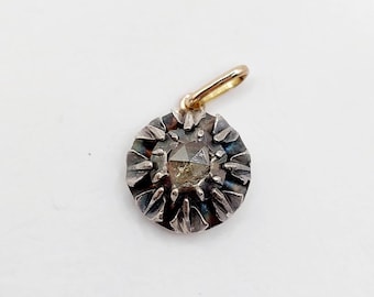 May include: A circular pendant featuring a central faceted stone set in a dark, oxidized silver-toned metal base with radiating petal-like prongs. A small, smooth gold-toned metal bail is attached to the top for hanging on a chain or cord.
