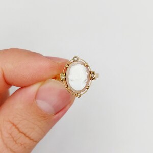 May include: A gold ring with a white cameo set in a gold frame with small pearl accents.