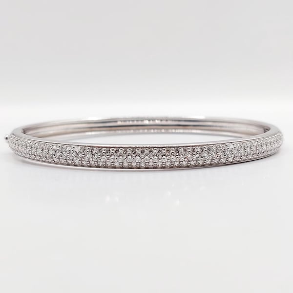 Pode incluir: Uma pulseira de prata com uma fila contínua de pequenas pedras preciosas transparentes. A pulseira é redonda e tem um design simples e elegante. As pedras preciosas são colocadas próximas umas das outras, criando um efeito brilhante.