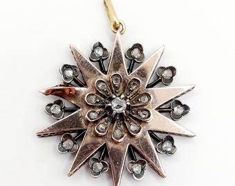 May include: A gold and silver star-shaped pendant with a central flower design set with small diamonds. The pendant is made of metal and has a loop at the top for hanging.