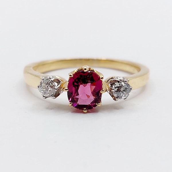 Pode incluir: Um anel de ouro com uma pedra central magenta oval e duas pedras claras redondas menores. O anel tem um design simples e elegante, adequado para uso diário ou eventos especiais. Uma joia clássica.