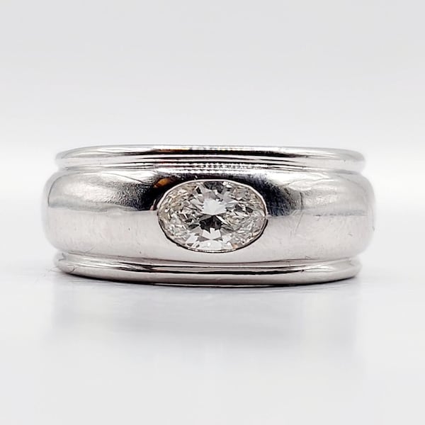 Pode incluir: Um anel de prata com um grande diamante de corte oval no centro. O anel tem uma banda larga com um acabamento polido e arredondado. O diamante brilha intensamente contra a prata.