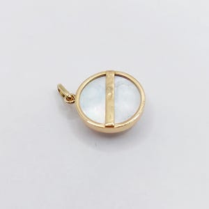 May include: A gold pendant with a round mother-of-pearl inlay and a gold bar across the center.