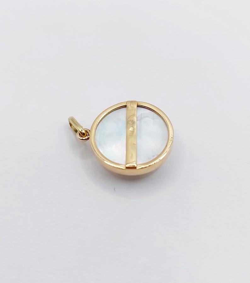 May include: A gold pendant with a round mother-of-pearl inlay and a gold bar across the center.