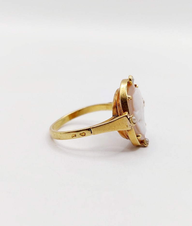 May include: A gold ring with a cameo set in the center. The cameo is a white shell with a carved portrait. The ring is set with small diamonds around the cameo.