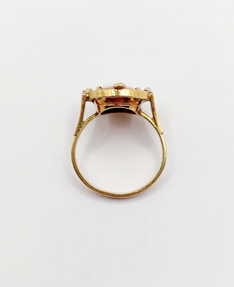 May include: A gold ring with a brown oval stone set in a bezel setting. The stone is surrounded by smaller diamonds.