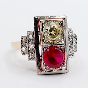 Peut inclure: Une bague vintage avec un sertissage rectangulaire, ornée d'un diamant jaune-vert et d'un rubis rouge. La bague a un anneau en or et est ornée de petites pierres précieuses claires sur les côtés.
