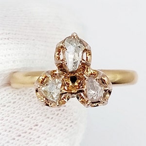 Könnte beinhalten: Ein goldener Ring mit drei Diamanten. Der zentrale Diamant ist im Marquise-Schliff, flankiert von zwei kleineren, birnenförmigen Diamanten. Die Fassung hat aufwendige Details, und das Band ist aus poliertem Gold.
