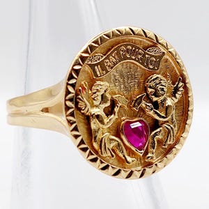 Anillo de amor vintage "Late por ti" oro rosa de 18k adornado con querubines esculpiendo un corazón de rubí sintético