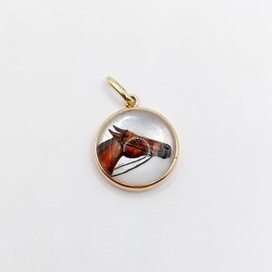 May include: A gold pendant with a clear glass cabochon featuring a painted image of a brown horse's head.