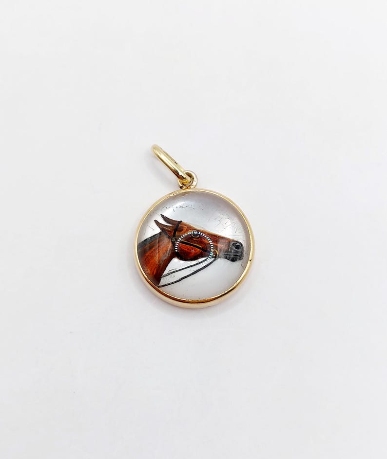 May include: A gold pendant with a clear glass cabochon featuring a painted image of a brown horse's head.