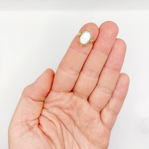 May include: A gold ring with a white cameo set in a gold frame with small gold beads around the edge.